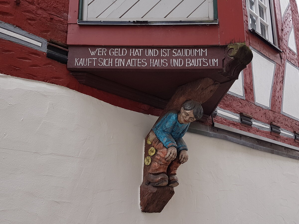 [Translate to Französisch:] In Holz geschnitzte Figur am Haus mit Spruch